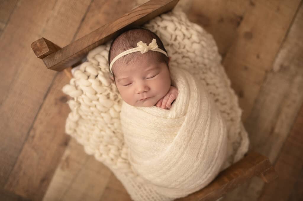 newborn girl posed asleep on a wooden bed prop