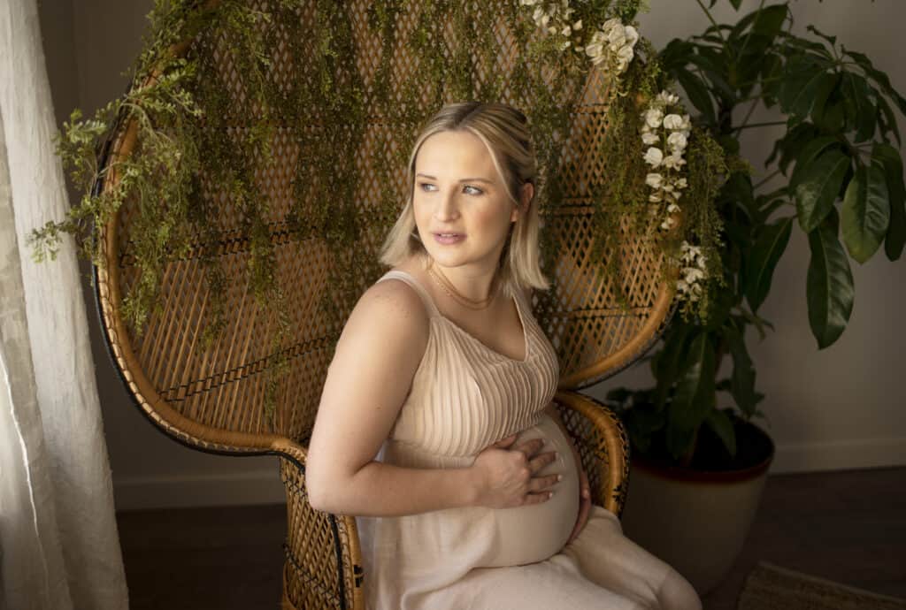 expecting mother holds belly in peacock chair