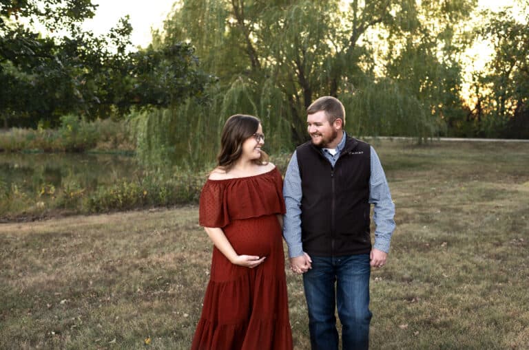 pregnant couple walks in a park holding hands