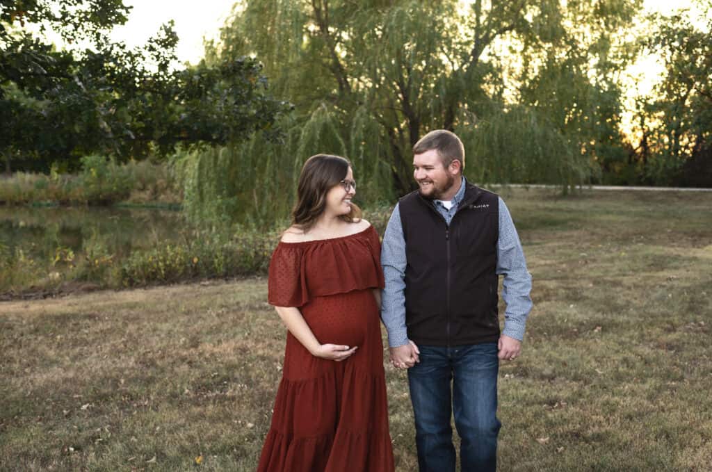 expecting couple walks in a park holding hands