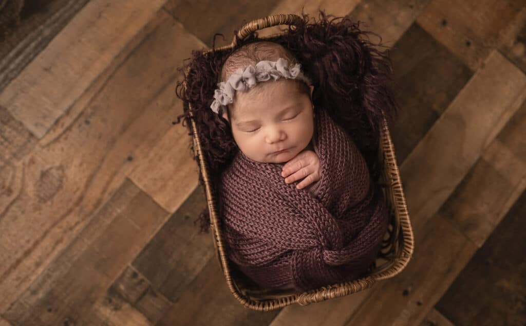 newborn baby girl wrapped in purple in a basket