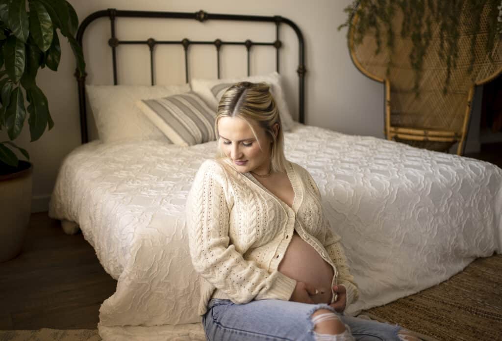 studio maternity photos mother sits next to a bed