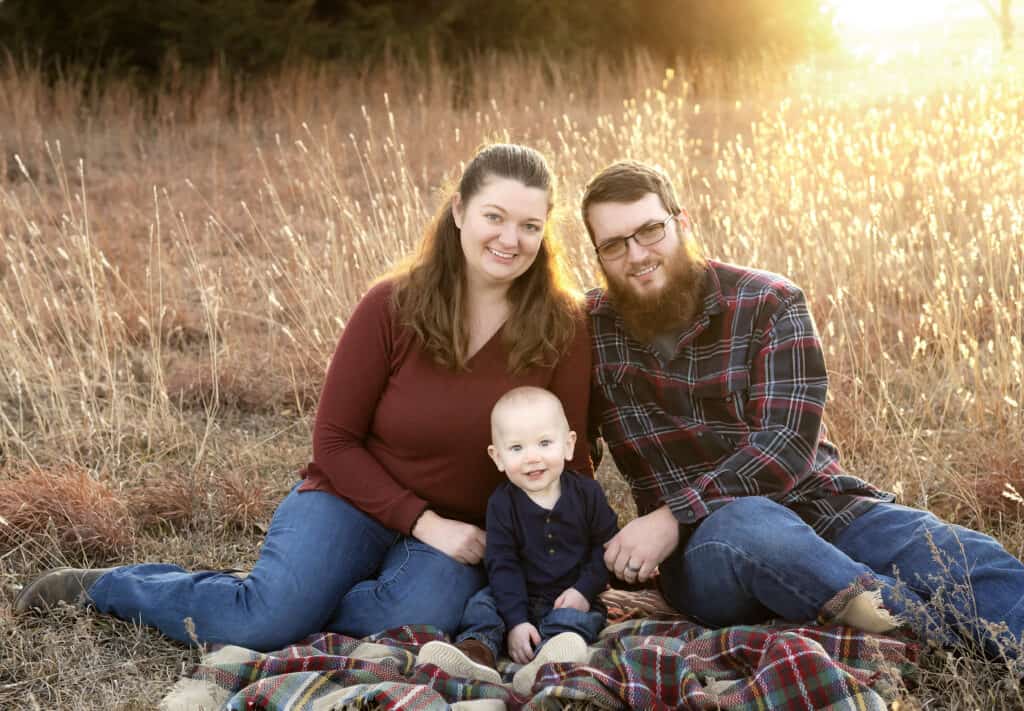 family of three sits on a blanket for family photos