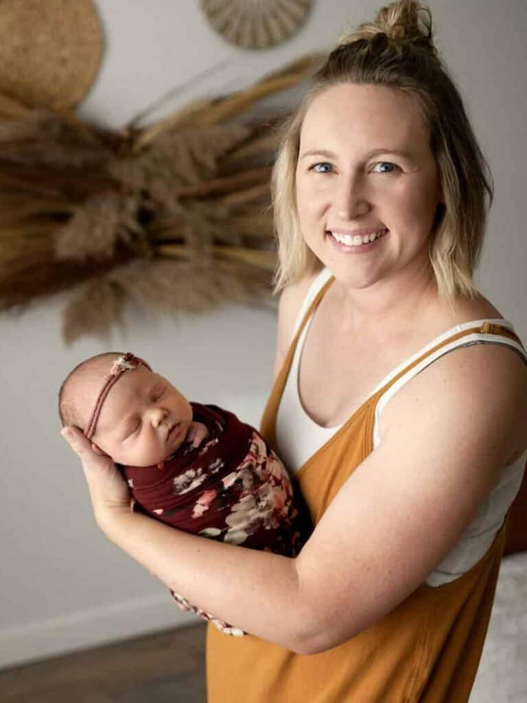 sara nuzum newton ks photographer holds a wrapped newborn during a session