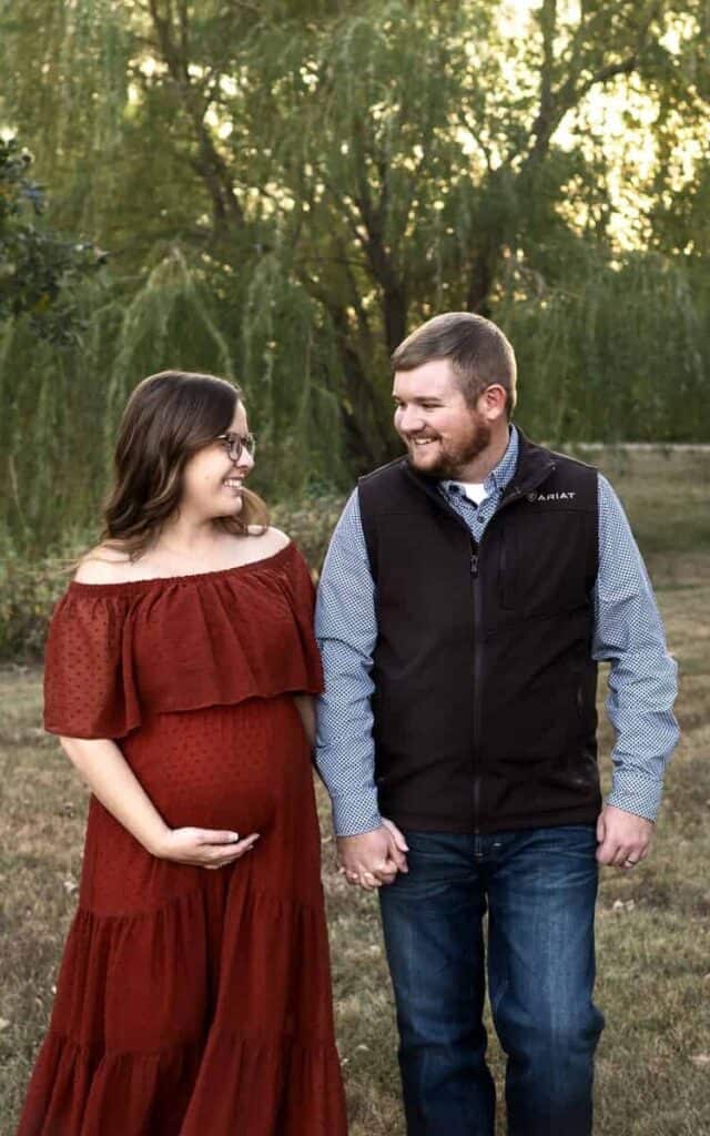 pregnant couple walks in a park holding hands